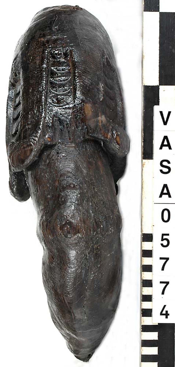 Del av skulptur. Arm till Stora krigaren på babord sida. Mycket kraftig. Bruten. Saknar hand samt en del av klädnadens ärm. Vackert snidad. Konstnären har använt sig av träets ådring för att få fram musklernas form.

Text in English: Arm belonging to sculpture. Very worn, broken.