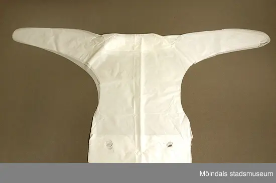 Tre (3) vita plastsnibbar som användes för att fästa småbarnsblöjor på barn. En utav snibbarna innehåller en blöja från blöjförpackning MM04256. Brukades troligen av Kerstin Olofsson till hennes barn på 1970-talet.