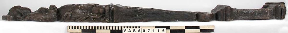 Skulpterad pilaster med övre delen i form av en karyatid med yppig, konstrik frisyr.
Höger arm hålls böjd med handen placerad framför bröstet. Vänster arm hålls utsträckt utefter sidan med handen vilande mot höften. Underkroppen döljs av ett hölje som framtill är prytt med stora, spiralformade ornament och små djurfigurer.
Karyatiden avgränsas från det rullverksornerade pilasterskaftet av en profilerad list. Nedtill avslutas skaftet av ett rullverksornament ovanför den rikt profilerade basen. Nedtill är pilastern försedd med en hög piedestal, prydd med beslagsornamentik. Figuren och dekoren omfattar även pilasterns sidor. Baksidan är slät.


Text in English: Sculpted pilaster with its upper part shaped as a Caryatid with a luxuriant artistic coiffure.
The right arm is held bent with the hand in front of the breast, the left arm is held at the side with the hand resting against the thigh. The lower part of the body is concealed by a shift or slip that is decorated with large spiral-shaped ornaments and small figures of animals.
A profiled batten separates the Caryatid from the shaft of the pilaster, which is ornamented with scrollwork. The shaft terminates with a scrollwork ornament above the richly profiled base. Below, the pilster is equipped with a high pedestal, decked with applied ornamentation. The back is smooth.
