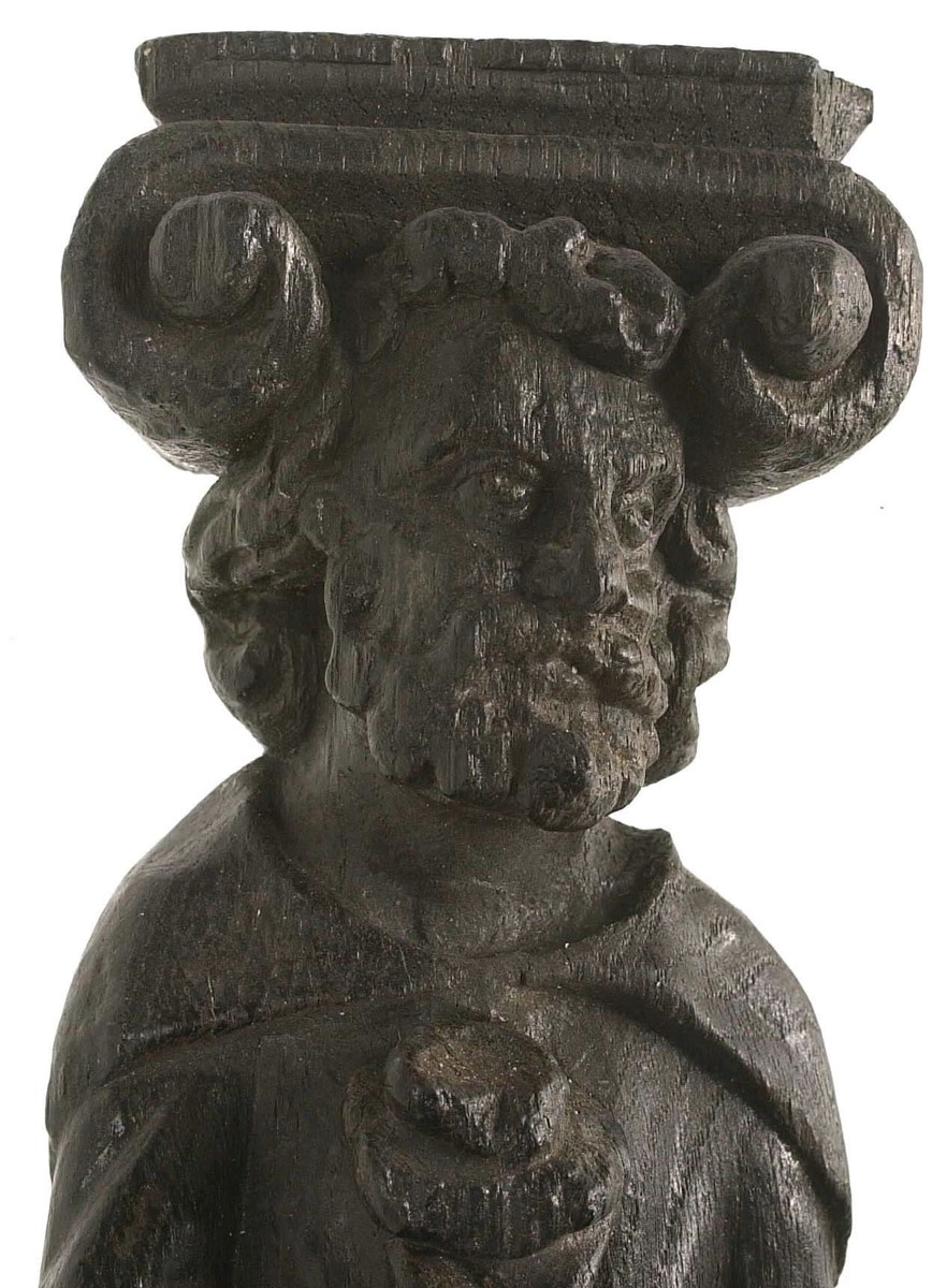 Hermpilaster.
Liten skulpterad pilaster föreställande skäggig herm under joniskt kapitäl.
Huvudet är vridet mot vänster. Hermen är insvept i en mantel som hålls fast med vänster hand framför magen. I höger hand håller figuren ett okänt föremål (blomsterkälk?) framför bröstet. Pilasterskaftet är prytt med stora frukter och blad, fasthängande vid en stängel som delvis täcker det nedåt avsmalnande skaftets ramverk. Baksidan är slät.
Skulpturen är mycket välbevarad med sju spikhål.

Text in English: Small sculpted pilaster with a bearded Herm beneath an Ionic capital.
The head of the figure is turned to the left. The Herm is enveloped in a mantle, held fast with the left hand in front of its stomach. Its right hand holds an unknown object (a bunch of flowers?) in front of its breast. The shaft of the pilaster is decked with large fruit and leaves hanging from a stalk which partly cover the framing of the tapering shaft. Its back is flat.
The sculpture is very well preserved.