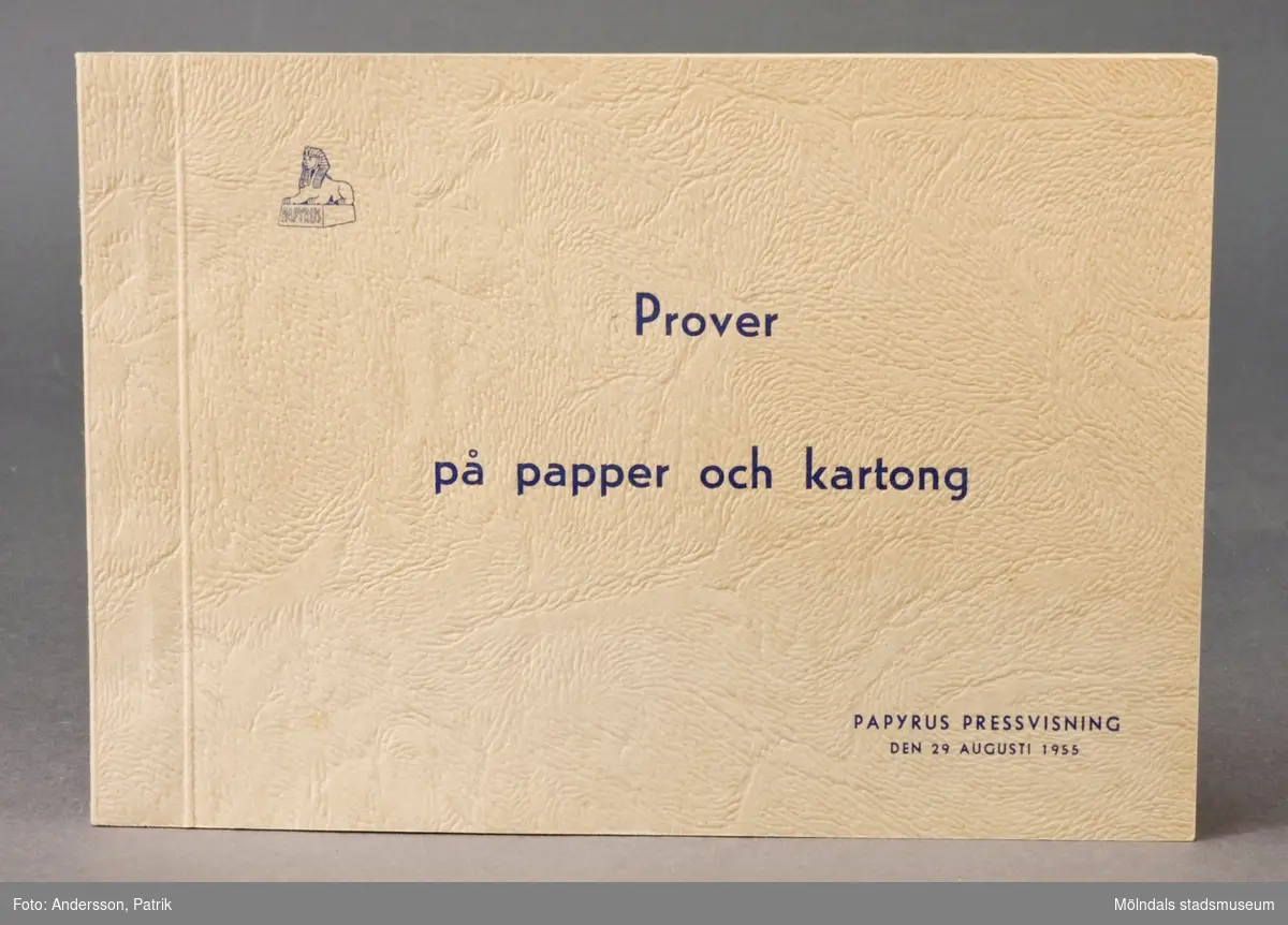 Häfte med prover på papper och kartong. Pärm av mönsterpressat grovt papper med blått tryck och Papyruslogotyp. Tillverkades för Papyrus pressvisning den 29 augusti 1955.