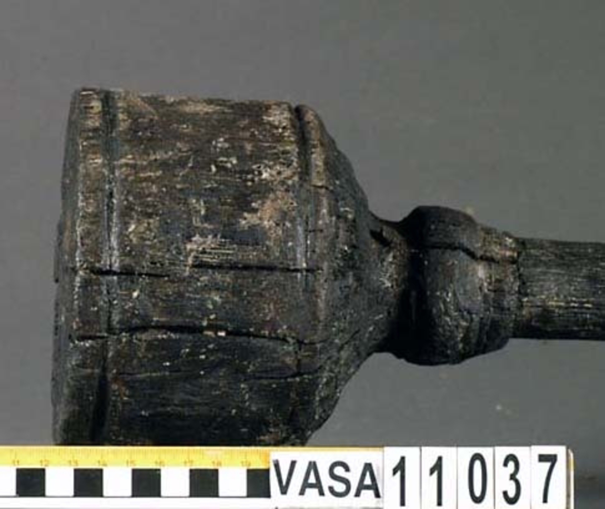 Kolv till ansättare. Kolven består av ett cylindriskt, svarvat, trästycke med ett centrerat skafthål. I övre änden, åt skaftet till, är kolven profilsvarvad. Motsatt ände är platt. Några sprickor, annars i fint skick.