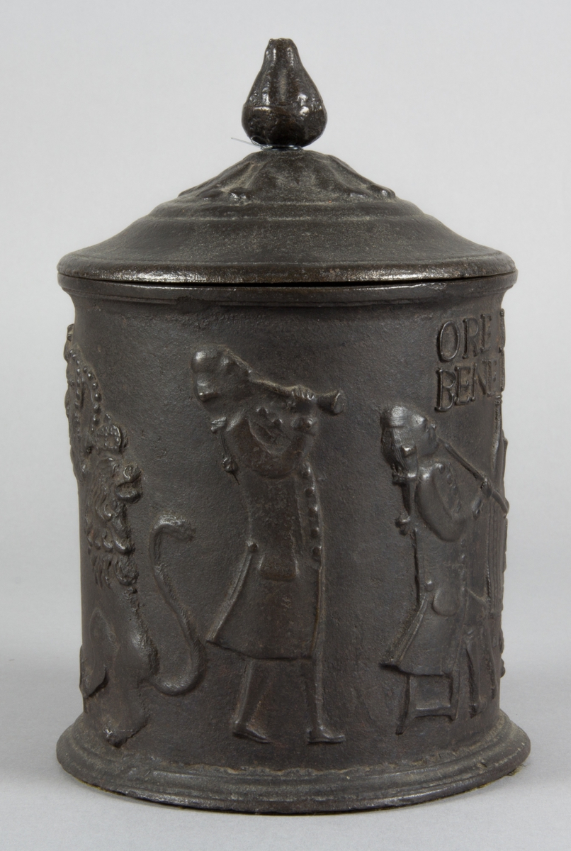 Relief på burken med text. Relief med rökande och spelande män. Några av männen sitter vid en spis. Riksvapen med flankerande lejon. Årtal 1794.
Text på burken. ORE FUMOSO BENE BIBENTUR.