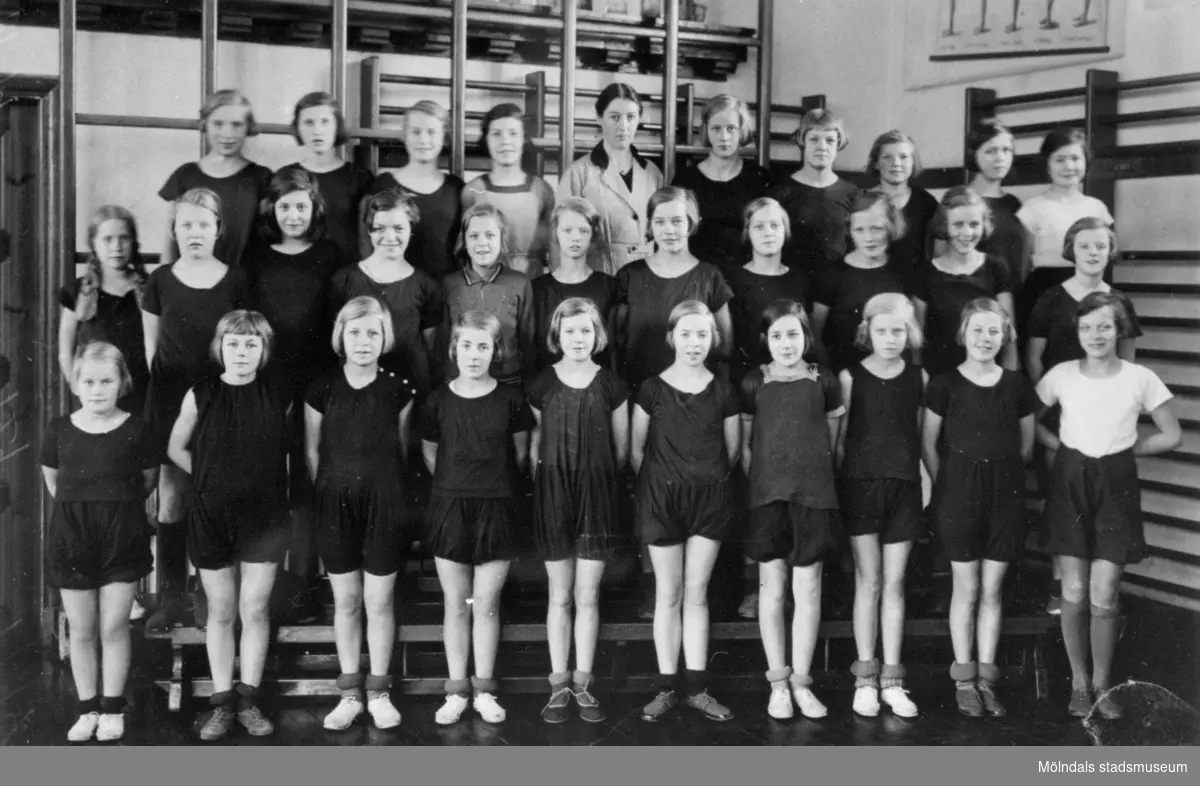 Gruppbild med flickor i gymnastikkläder uppställda i gymnastiksal på Kvarnbyskolan i Mölndal ca 1934.