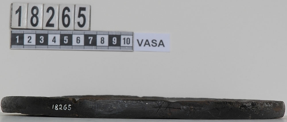 En svarvad trädisk. Disken har fem bomärken, två sitter på diskens ena sida, ett på andra sidan samt två stycken längs kanten.