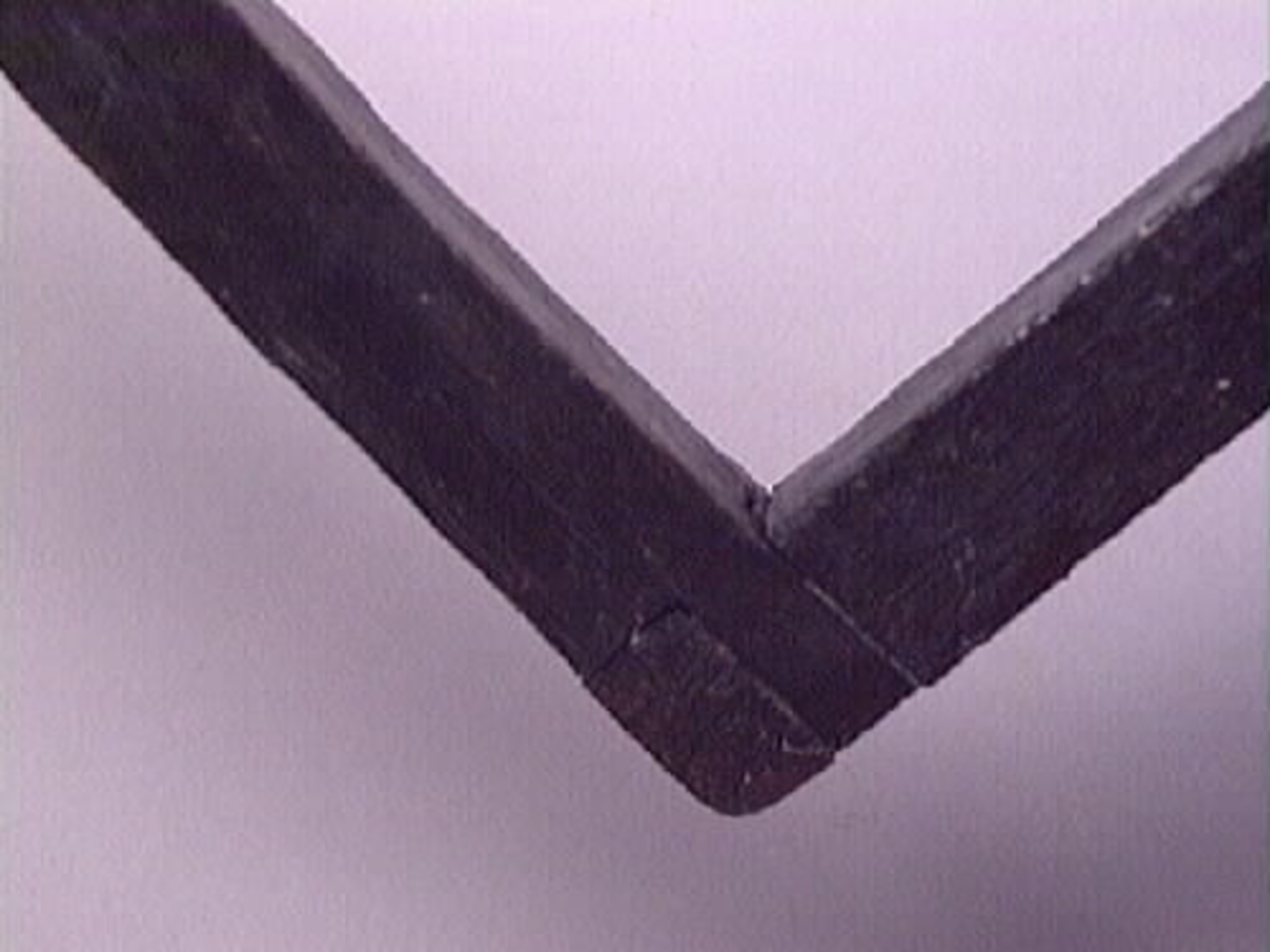 En vinkelhake.

Vinkelhaken består av två plana stavar som är sammanfogade genom sinkning. Ändarna är profilerade. I mitten av den kortare staven finns ett runt hål för upphängning.

Vinkelhaken är välbevarad och i gott skick.

För mer information se Dokumentationsblankett under Referenser – Länkade filer.