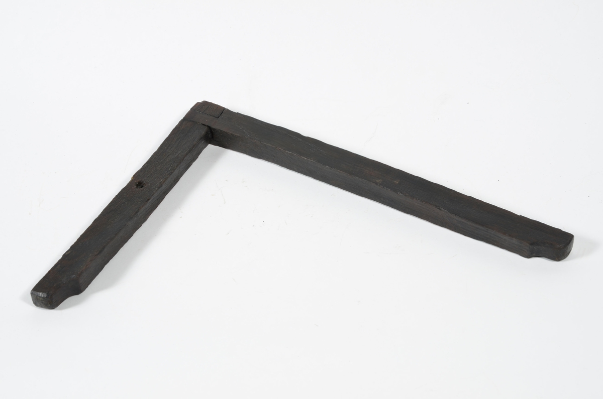 En vinkelhake.

Vinkelhaken består av två plana stavar som är sammanfogade genom sinkning. Ändarna är profilerade. I mitten av den kortare staven finns ett runt hål för upphängning.

Vinkelhaken är välbevarad och i gott skick.

För mer information se Dokumentationsblankett under Referenser – Länkade filer.