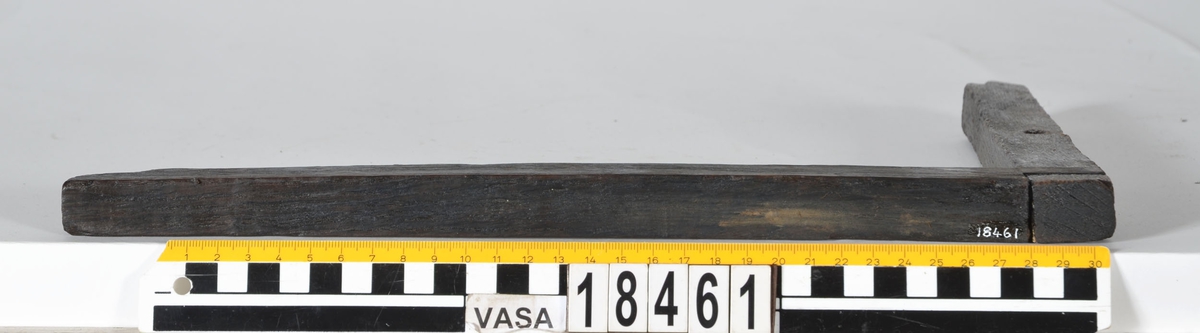 En vinkelhake.

Vinkelhaken består av två plana stavar som är sammanfogade genom sinkning. Ändarna är profilerade. I mitten av den kortare staven finns ett runt hål för upphängning.

Vinkelhaken är välbevarad och i gott skick.

För mer information se Dokumentationsblankett under Referenser – Länkade filer.