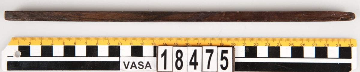 En tumstock av trä.

Tumstocken är försedd med elva inristade skåror som markerar tolv tum. På den mittersta skåran finns ett inristat kryss. Ytterligare ett kryss, dock något mindre, har ristats in vid skåran närmast mittskåran.

Tumstocken är i gott skick.

För mer information se Dokumentationsblankett under Referenser – Länkade filer.