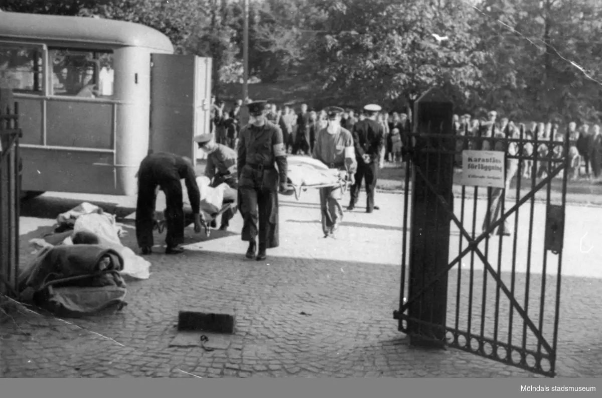 "Karantänsförläggning" på Kvarnbyskolan för överlevande från koncentrationsläger i Tyskland och Polen 1945.  
Skolan fungerade under denna sommar som beredsskapssjukhus.

Flyktingar bärs in på bår av Röda Korsets personal.