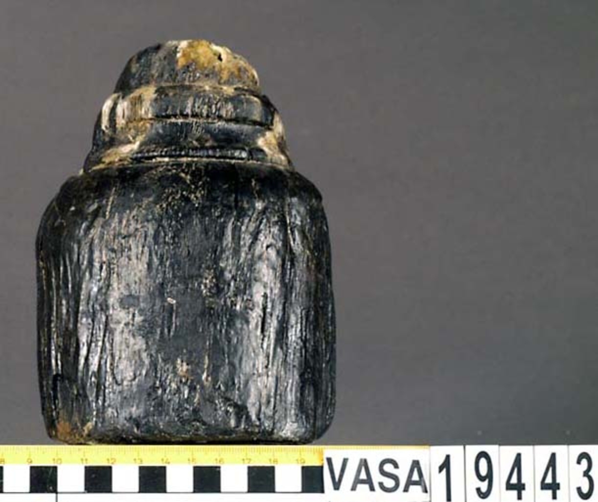 Kolv till ansättare. Kolven består av ett cylindriskt, svarvat, trästycke med ett centrerat skafthål. I övre änden, åt skaftet till, är kolven profilsvarvad. Kolven är kraftigt eroderad, mest på ena sidan. En kraftig spricka från utsidan in till skafthålet.