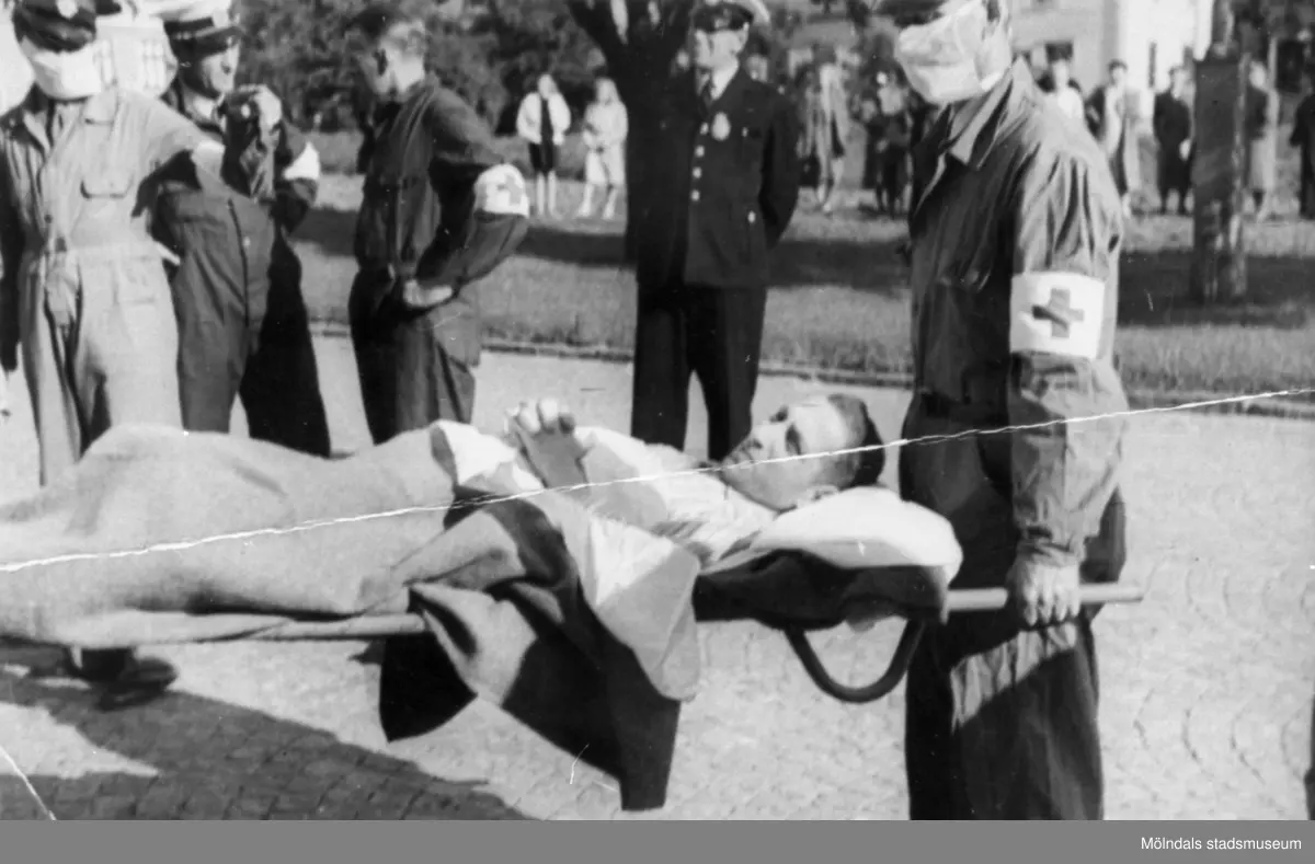 "Karantänsförläggning" på Kvarnbyskolan för överlevande från koncentrationsläger i Tyskland och Polen 1945.  
Skolan fungerade under denna sommar som beredsskapssjukhus.
 
Flykting som blir buren på bår av Röda Korsets personal.