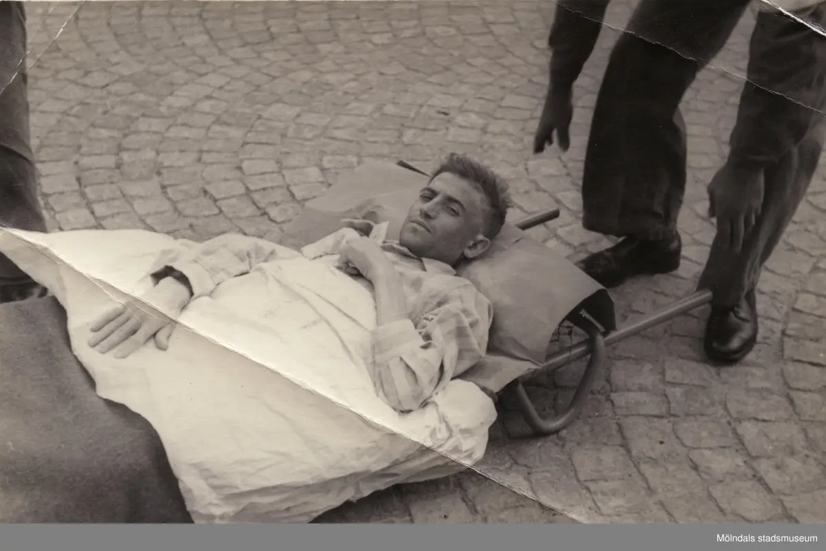 "Karantänsförläggning" på Kvarnbyskolan för överlevande från koncentrationsläger i Tyskland och Polen 1945.  
Skolan fungerade under denna sommar som beredsskapssjukhus.
 
Manlig flykting som bärs på bår.
