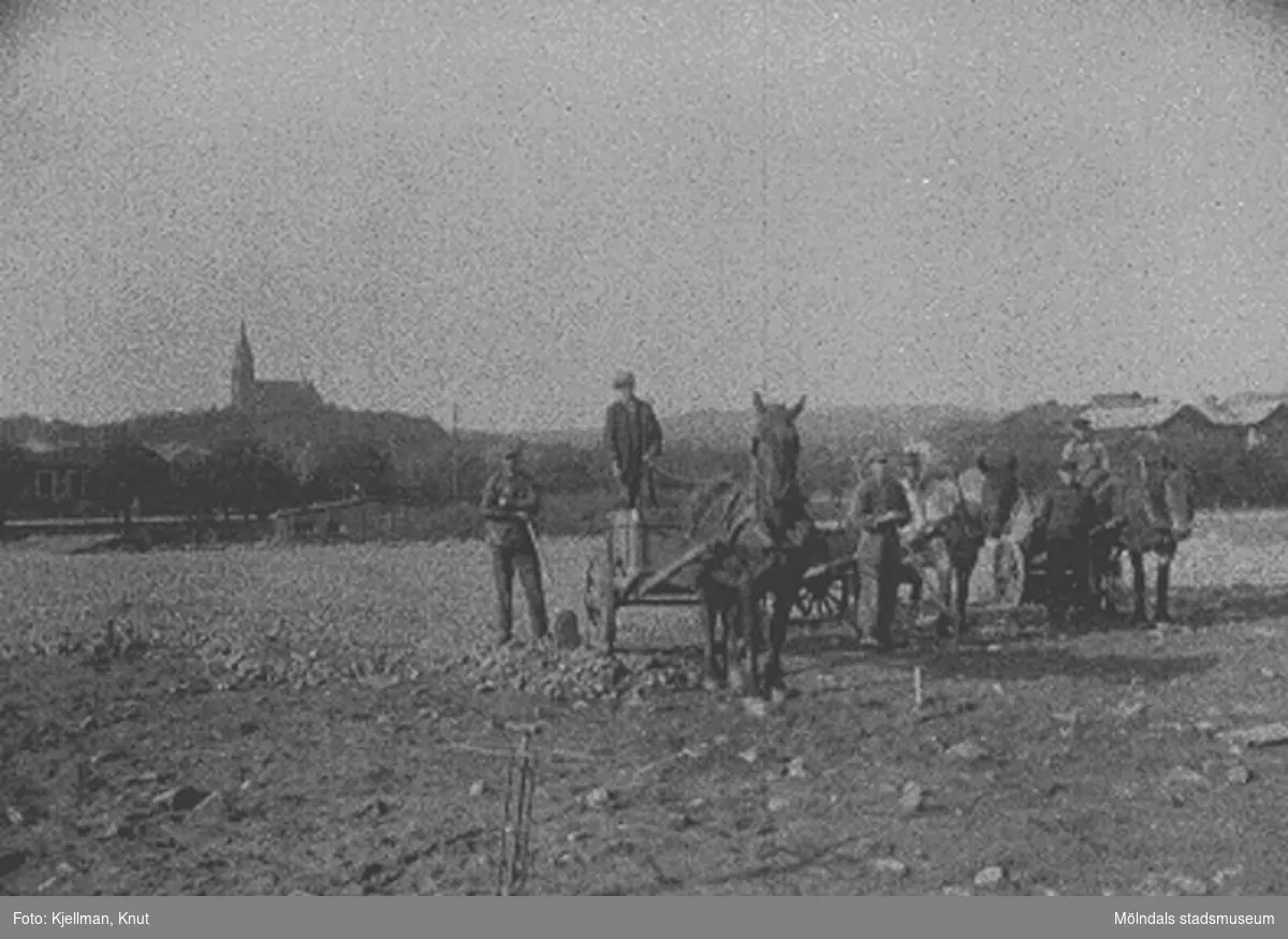 Nya torget (nuvarande Gamla torget) anläggs i Mölndal kvarnby 1924-1925. Nödhjälpsarbetare strör makadam över marken. Tredje mannen från vänster är Oskar Lund med hästen Grållen. Längst ut till höger står Korgmakar’ns Knut. I bakgrunden skymtar längst till vänster spårvagnsstallarna vid Göteborgsvägen, och längst till höger ses Svalövsbolagets lagerbyggnad och järnvägsstationen Mölndals Nedre. Nya torget finns inte sedan 1974, och alla de nämnda byggnaderna är rivna. Fässbergs kyrka, syns längst bak, är det enda som återstår.