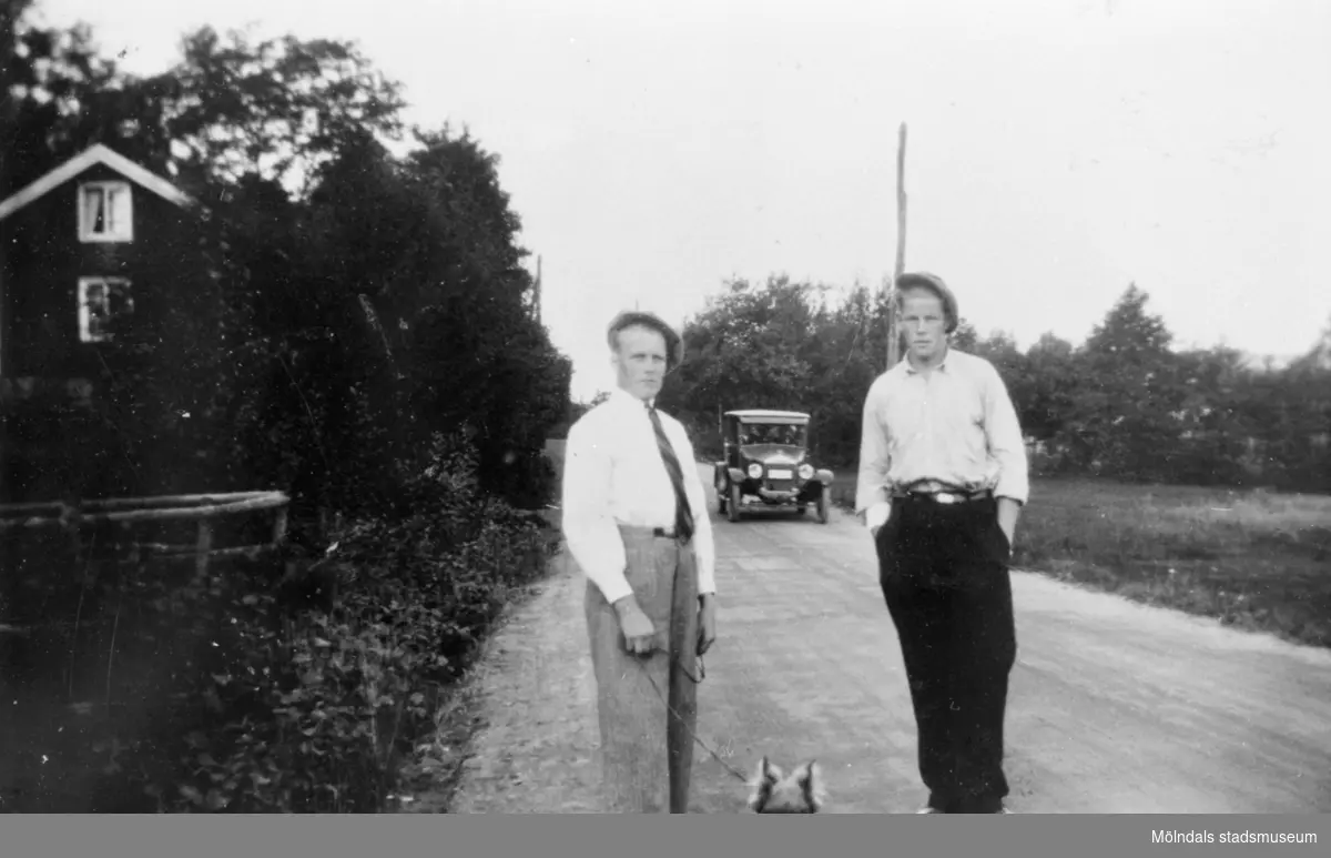 Arvid och Gustav med hund utanför sitt hem Antons, 1930-talet. En tidstypisk bil kommer bakom.