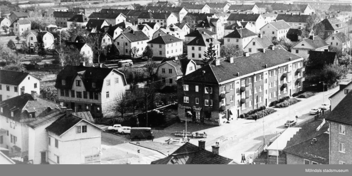 Vy från Fässbergs kyrka över Broslättsområdet/Mölndals centrum. 
Åt vänster i förgrunden ses Frölundagatan (nu Brogatan) och Storgatan åt höger. I bildens nedre vänstra hörn syns huset med Andren´s Möbler (gatunr 28) och därbredvid huset som kallades "Biljarden" (Frölundagatan 26). I bildens centrum ligger Berghedes Blommor, Frukt och Kiosk. Vid nedfälld markis: Dolemans Bageri.