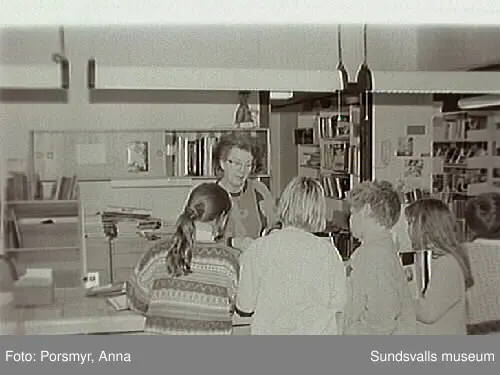 Dokumentationsfotografering av verksamheten vid biblioteksfilialen i Matfors. Bild 01Biblioteksassistenten Ingrid Engström, Matfors bibliotek, med låntagare vid utlånedisken. Bild 09 bibliotekaren Inger Barkman läser för en grupp förskolebarn i bibliotekets "läsrum".