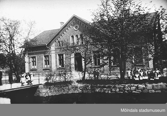 Två barn står på bron som går över Kvarnforsen. Utanför skolan står fler elever.