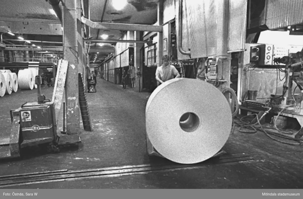 En arbetare med en pappersbal.
Bilden ingår i serie från produktion och interiör på pappersindustrin Papyrus, 1980-tal.