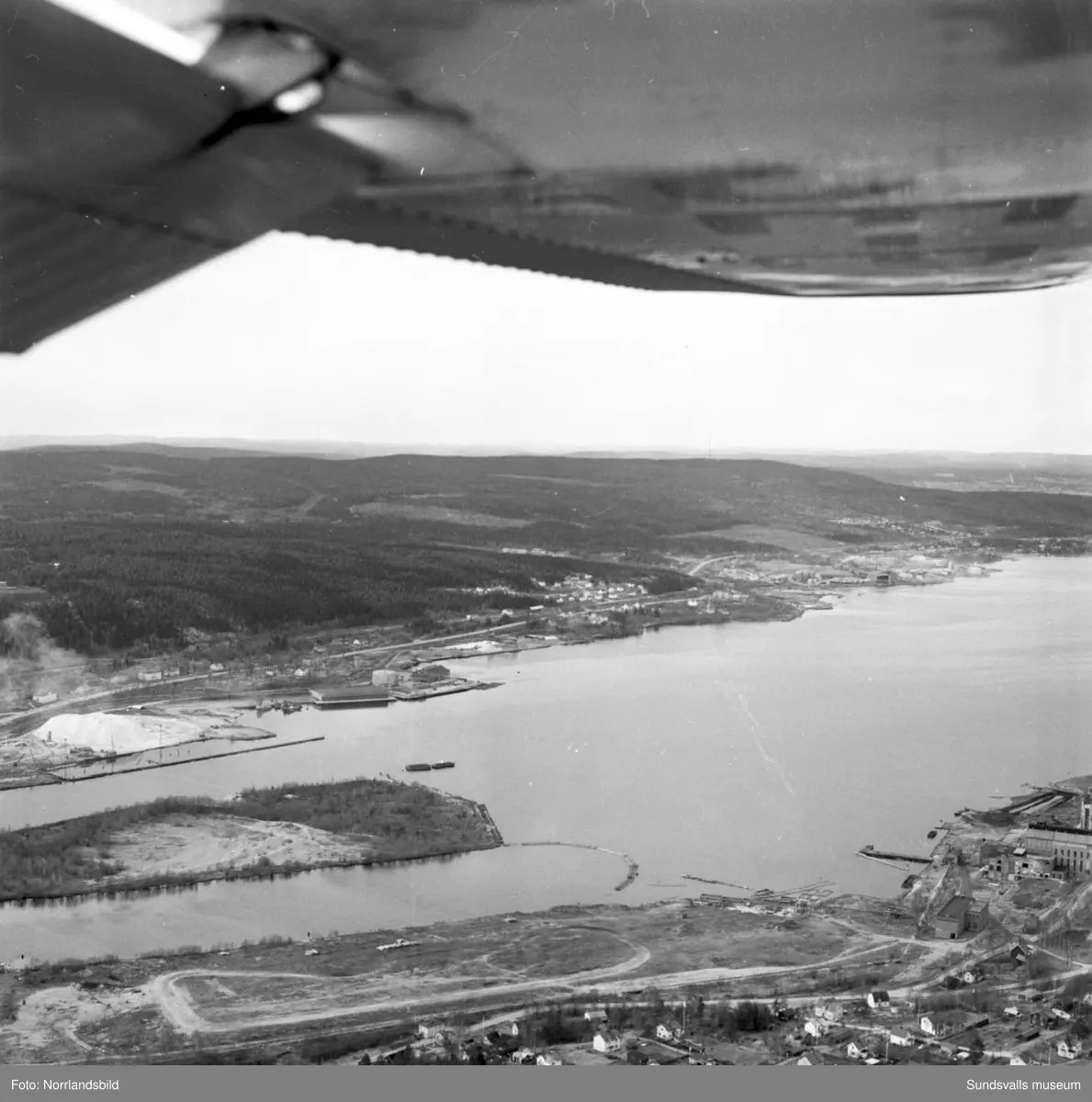 Flygfoton över Essvik och Nyhamn med timmerupplag och fabriksbyggnader.