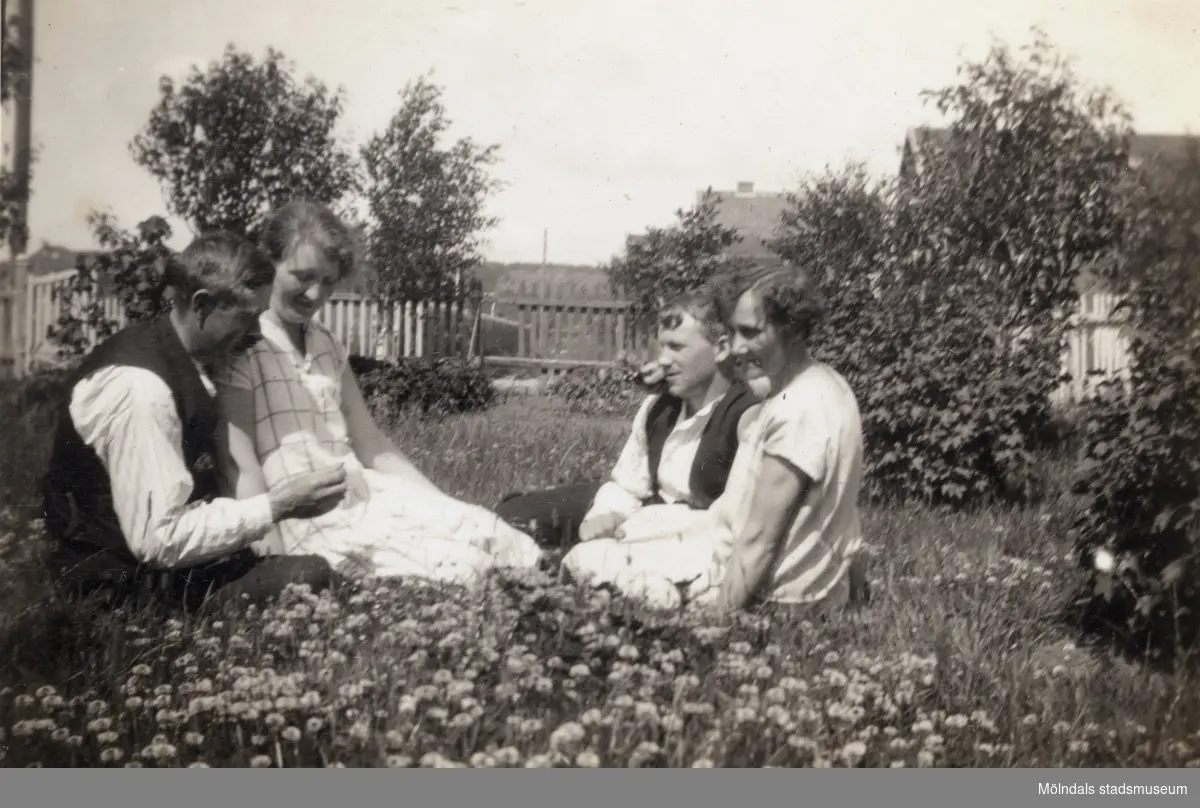 Fyra personer fotograferade sittande i trädgården till Solhemsgatan 10. Fotografi ur album som tillhört Hilda Börjesson Hallgren.