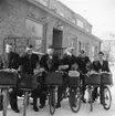 Cyklande lokalbrevbärare i Ljungby på väg ut med post i april 1955. I bakgrunden postkontoret.