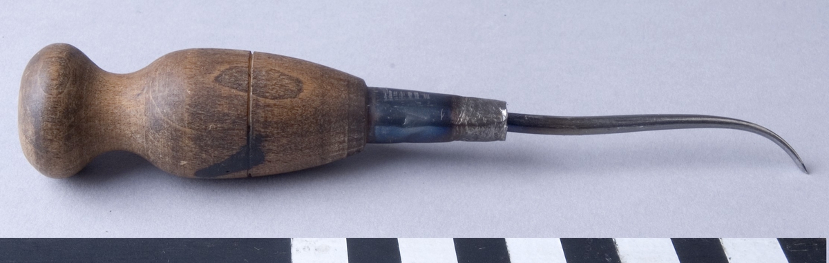 Syl, flatsyl, med syl av stål samt med svarvat handtag av trä. Sylen är fäst i handtaget med hjälp av en metallhylsa och är böjd framtill med slipat platt skär.