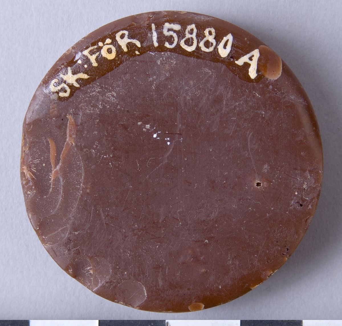 Färgvax, två stycken runda kakaor av vax i brun kulör. Märkt: "AJAX WAX" , "BOSTON BLACKING CO" samt med en figur i form av en gladiator.

A: med små nagg i kanten
B: med ett stort nagg i kanten samt med hål efter luftbubblor i  botten.