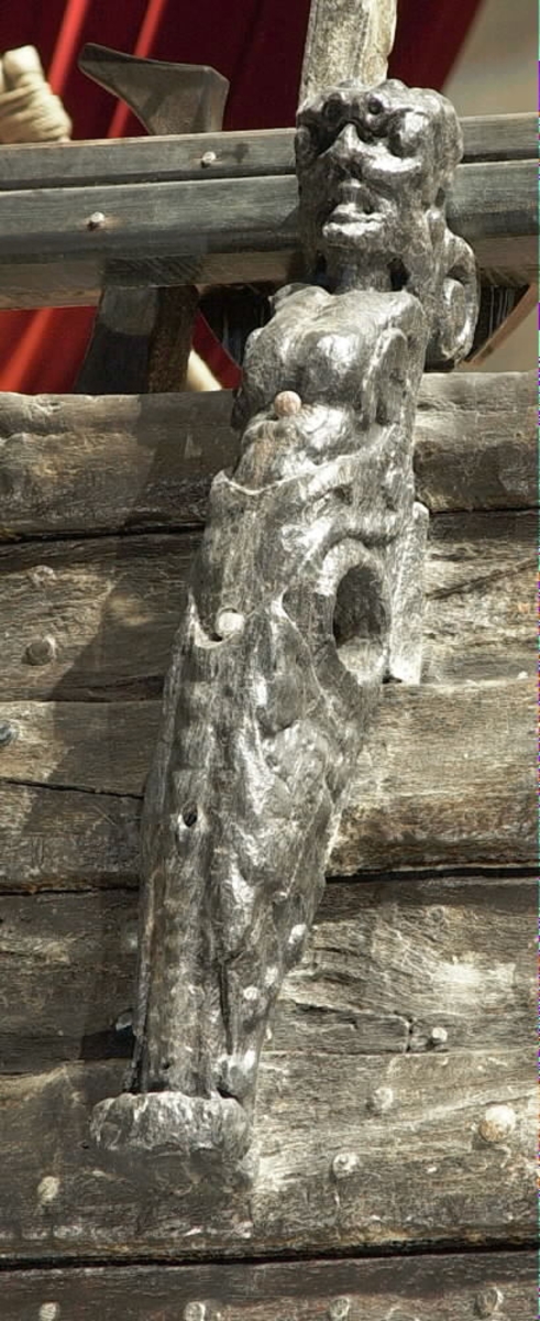 Skulptur i form av en slätrakad herm med öppen mun och stor, bred näsa.
På hjässan sitter ett djurhuvud troligtvis föreställande ett lejon. Armar är ersatta av upprullade bladslingor. Hermens nederdel är formad till ett fodralliknande "hölje" prytt med bladslingor. Ornamentiken är av organisk karaktär med större och mindre, elegant formade bladslingor. Nedtill är "höljet" upprullat till en vulst. Sedd från sidan är hermen avsmalnande nedtill.
Baksidan, som har utgjort anliggningsyta, är försedd med ett antal stora urtag i höjd med hermens hjässa, bröstparti samt från midjan och nedåt. I midjehöjd återfinns även ett högsmalt urtag utmed baksidans ena hälft. Strax nedanför midjan går sidledes ett stort hål tvärs igenom skulpturen.
Skulpturen är delvis kraftigt sliten och finare detaljer i utförande har därför gått förlorade.

Text in English: Sculpture in the form of a clean-shaven Herm with open mouth and large, broad nose.
On top of his head is the head of an animal, possibly a lion. The arms have been replaced by strands of rolled-up leaves. The lower part of the Herm is sheathed in a "cover", decorated with leaf strands. The bottom of the "cover" is rolled up into a torus. Its ornamentation is of a pronounced organic character, with larger and smaller chains or festoons of leaves. Seen in profile, the Herm tapers downwards.
The back, also the attachment surface, has a number of large cut-out holes on the same level as the Herm''s head, chest, waist and further down. At one side of the back of the waist there is also a narrow vertical groove. Just below the waist, a large hole passes through the Herm.
The sculpture is very worn in places and any finer details have been lost.