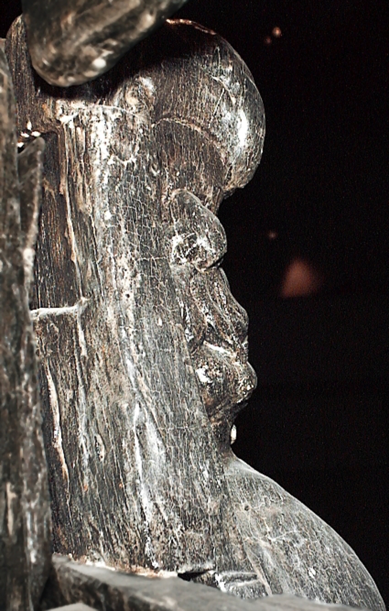 Skulptur av en triton, svängd mot höger.
Tritonen är framställd i vänster profil och avtecknar sig i hög relief mot det släta bakstycket. Tritonen har en stor näsa och treflikig mustasch. På huvudet sitter en hjälm med dekorativa bladvoluter. Armarna är ersatta av långa, flikiga bladslingor. Bålens övergång i den fjällförsedda fiskstjärten markeras av stora bladbildningar. Tritonens stjärt döljs bakom stjärten och vingen till en under liggande drake, se fyndnummer 21277. På baksidan finns urtag för relingslisten.
Skulpturen är mycket välbevarad.

Text in English: A sculpture of a Triton curved to the right.
The figure is seen in left profile, in high relief against a plain back board. The face has a large nose and a moustache that splits into three parts. On its head is a helmet with decorative leaf volutes. The arms are replaced by long, lobed leaf formations. The transition area between the male torso and the scaled fish-tail is decorated with large leaves. The rear is hidden behind a dragon''s coiled tail and broad wing situated below, see No. 21277. There are notches on the back that fit into the railing.
The sculpture is very well preserved.