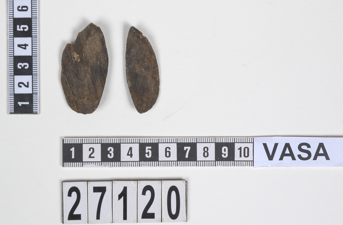 Två delar av en träsked. Delarna utgör mindre partier av skedbladet. På delarna syns en svagt rödbrun färg, vilket möjligen är spår efter bemålning.

Delarna är mycket slitna.

För mer information se Dokumentationsblankett under Referenser – Länkade filer.