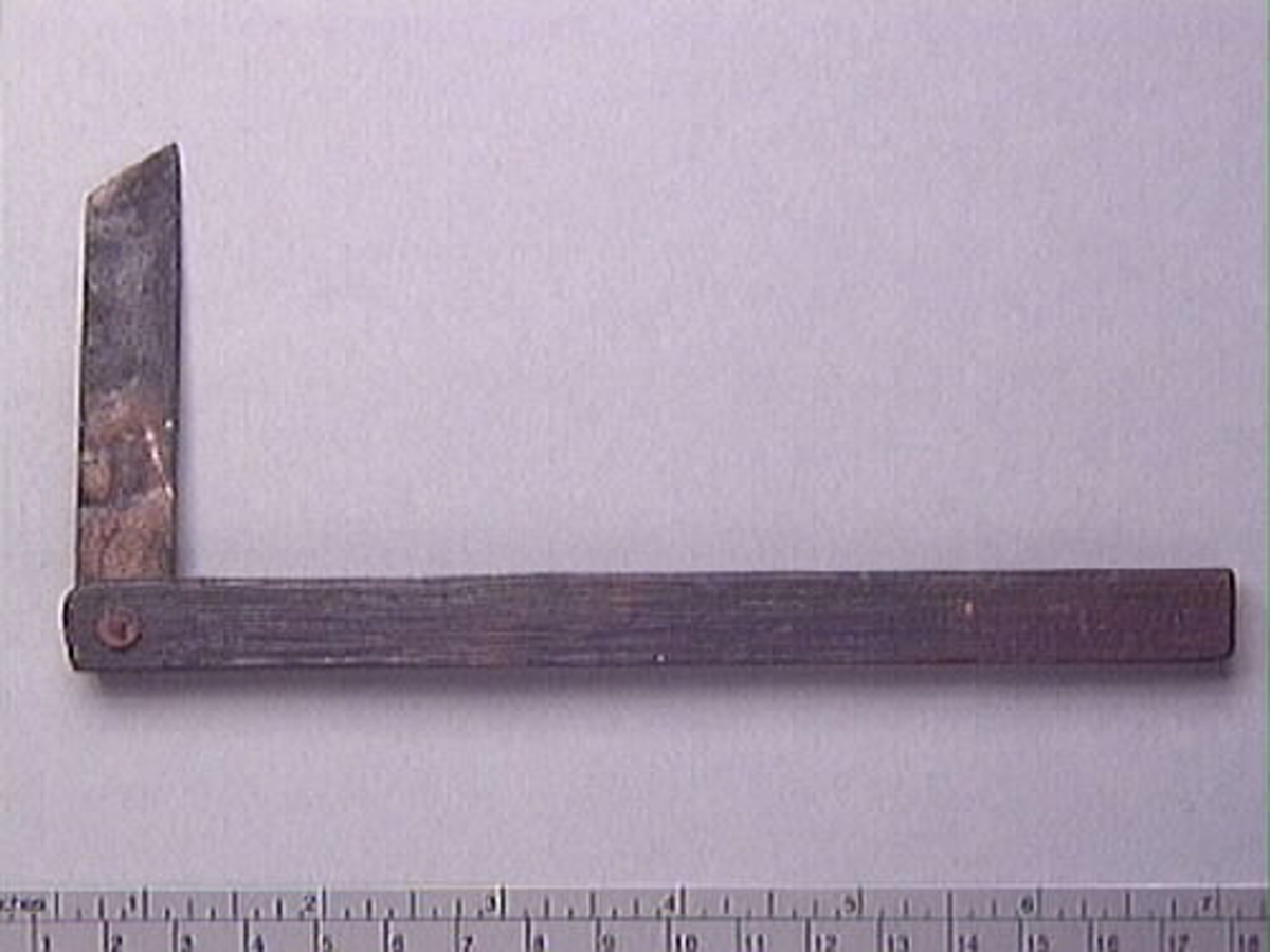 En vinkelhake, s k smygvinkel.

Skaftet är försett med sex stycken ristade skåror som markerar tum. I ena skaftänden sitter ett nytillverkat, ledat, järnblad. Bladet är fäst med en nytillverkad järnsplint. I skaftets ena ände, närmast bladet, löper en skåra eller ett spår. Spåret är mellan 68 och 80 mm djupt.

Smygvinkeln är i gott skick.

För mer information se Dokumentationsblankett under Referenser – Länkade filer.