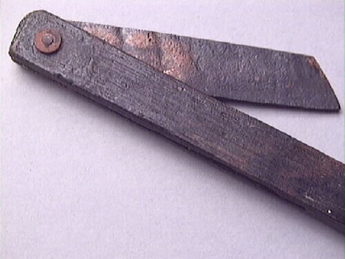 En vinkelhake, s k smygvinkel.

Skaftet är försett med sex stycken ristade skåror som markerar tum. I ena skaftänden sitter ett nytillverkat, ledat, järnblad. Bladet är fäst med en nytillverkad järnsplint. I skaftets ena ände, närmast bladet, löper en skåra eller ett spår. Spåret är mellan 68 och 80 mm djupt.

Smygvinkeln är i gott skick.

För mer information se Dokumentationsblankett under Referenser – Länkade filer.