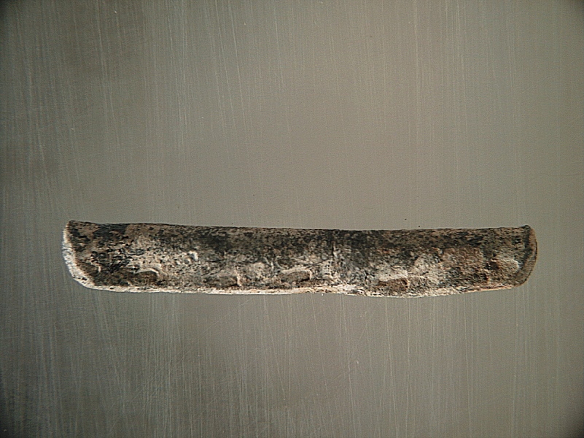 Sänket består av vikt blybit. Sänket har tydliga märken efter det verktyg som pressat ihop sänket runt garntråden. Sänket är i gott skick.

Text in English: Lead sinker in the shape of a flat tube. The rectangular piece of lead is folded vertically in half and has visible tool marks from the folding process. The yarn is pushed through the hole. Grey mat in colour. In good condition.