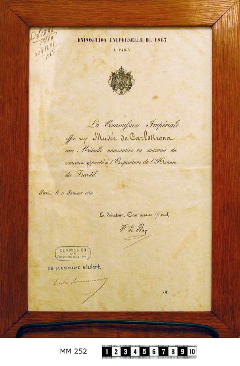 Medalj och diplom som tilldelats örlogsvarvets i Karlskrona utställning av fartygsmodeller mm vid utställningen i Paris år 1867. Medaljen i särskilt etui Diplomet inom ram av ek, polerad. Tillkom år 1868.
