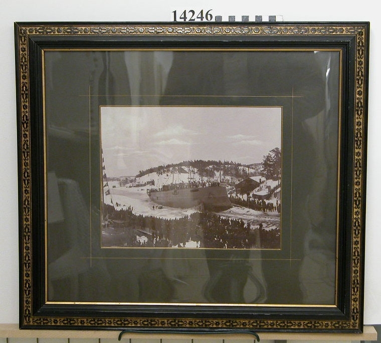 Fotografi inom glas och ram. Motiv: Pansarbåten Thules sjösättning. Text på baksidan: Pansarbåten Thules aflöpning vid Finnboda Slip d 4 Mars 1893.