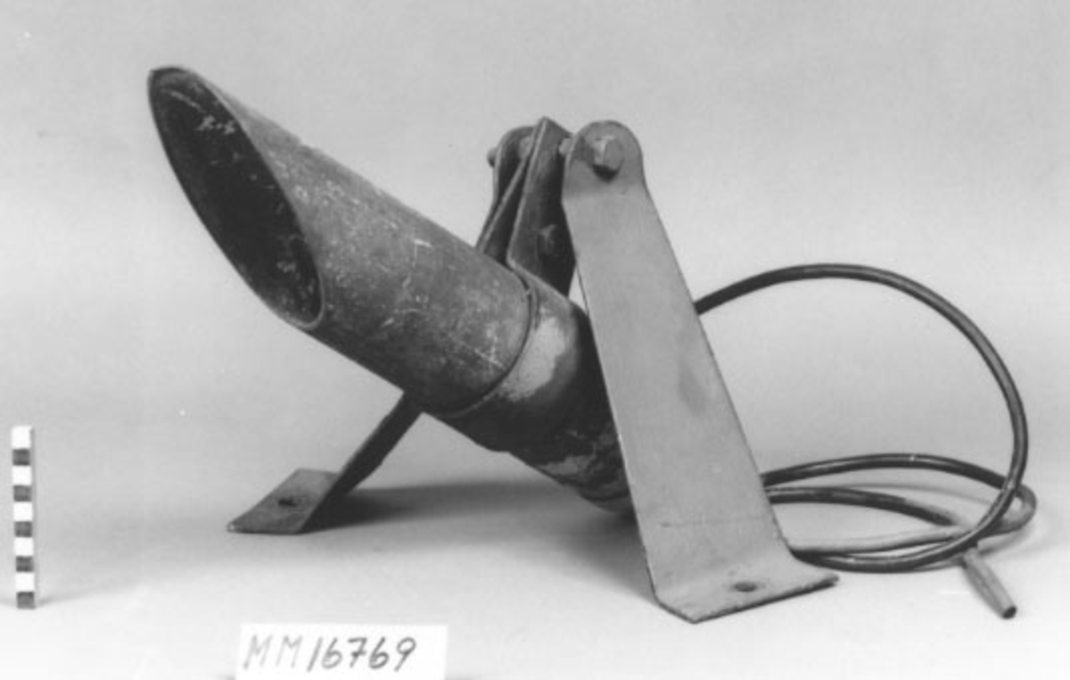 Cylinderformad kåpa med snedskuren öppning avskärmar lampan, fästad på arm av plattjärn. Kabelintag i andra änden. Målad i grått.