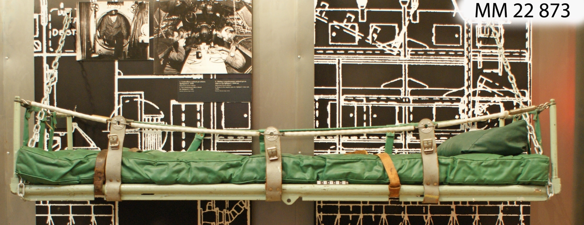 En ram av 30 mm tjockt stålrör som i sina hörnor har sängstolpar av 20 mm tjocka nedfällbara rör. Sängbotten av metallkedjor av galvaniserat järn. Längs sidorna kan kättinglängder fästas upp på sängstolparnas toppar. Kättingarna är klädda med plaströr och sammanlänkade med sängramen med flera korta vertikala läder- och plastband.
Madrass och liten kudde är galonklädda och försedda med isydda knappar (madrass 37 st, kudde tre st). Två beslagsband i form av tvådelade remmar finns på långsidorna.