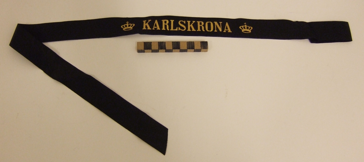 Mössband till rundmössa för manskap vid flottan.  Av svart rips med namn "KARLSKRONA" i guldbokstäver, flankerat av två kungl. kronor i guld. 7st olika mössband i samma förpackning. Alla från samma givare. Inventariebilagan ligger under MM 24615.