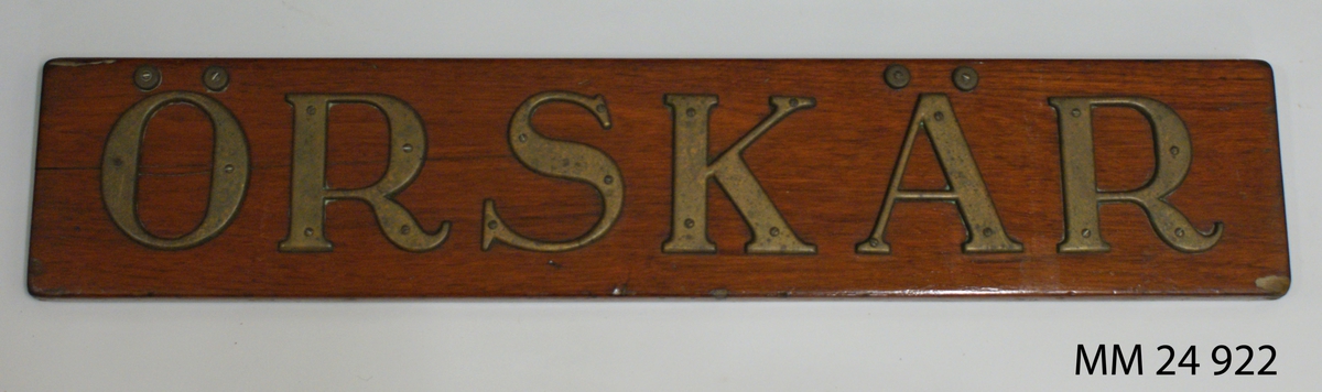 Namnbräda av teak, fernissad. Bokstäver av mässing med serif. Bokstäverna är fastskruvade från framsidan och bildar namnet: "Örskär".