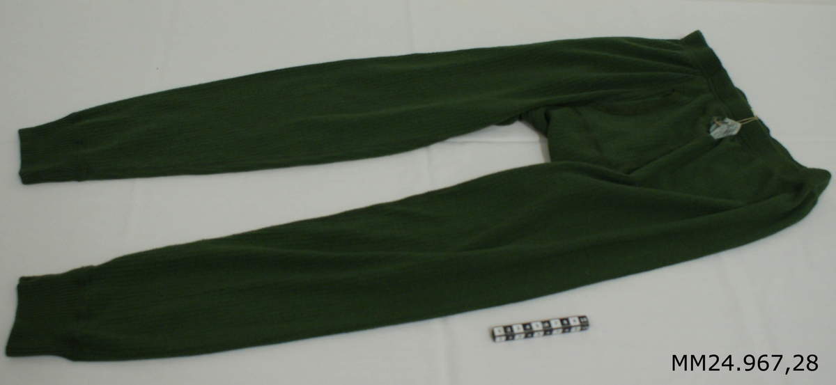 Långkalsong modell 1991. Grön kanalstickad långkalsong av polyester, bomull och cordelan. Resår i midjan samt omlottöppning vid gylfen. Kanalstickningen gör att en luftspalt till huden skapas vilket gör att fukten inte kommer när huden. Vitlapp på insidan med kronstämpel, M-nummer, tvättråd, årtalet 2000, storlek 4, vikt 60-70 kg samt texten: "Eiser Trikå Ab, tillverkad i Estland".