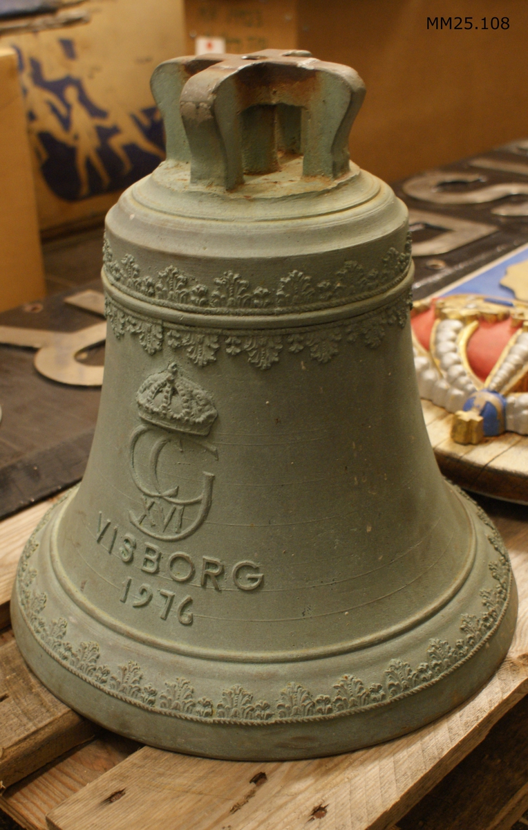 Skeppsklocka med ornamentering längs klockans topp och botten. Mitt på klockan text i relief: "VISBORG 1976" under Karl XVI Gutsavs monogram.