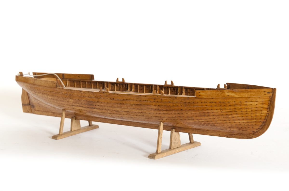 Gigg, bordlagd på spant, klink med fullständig inredning. 6 årtullar, 6 åror. Roder med skädda. Fernissad, Stativ fernissat. Masten saknas.