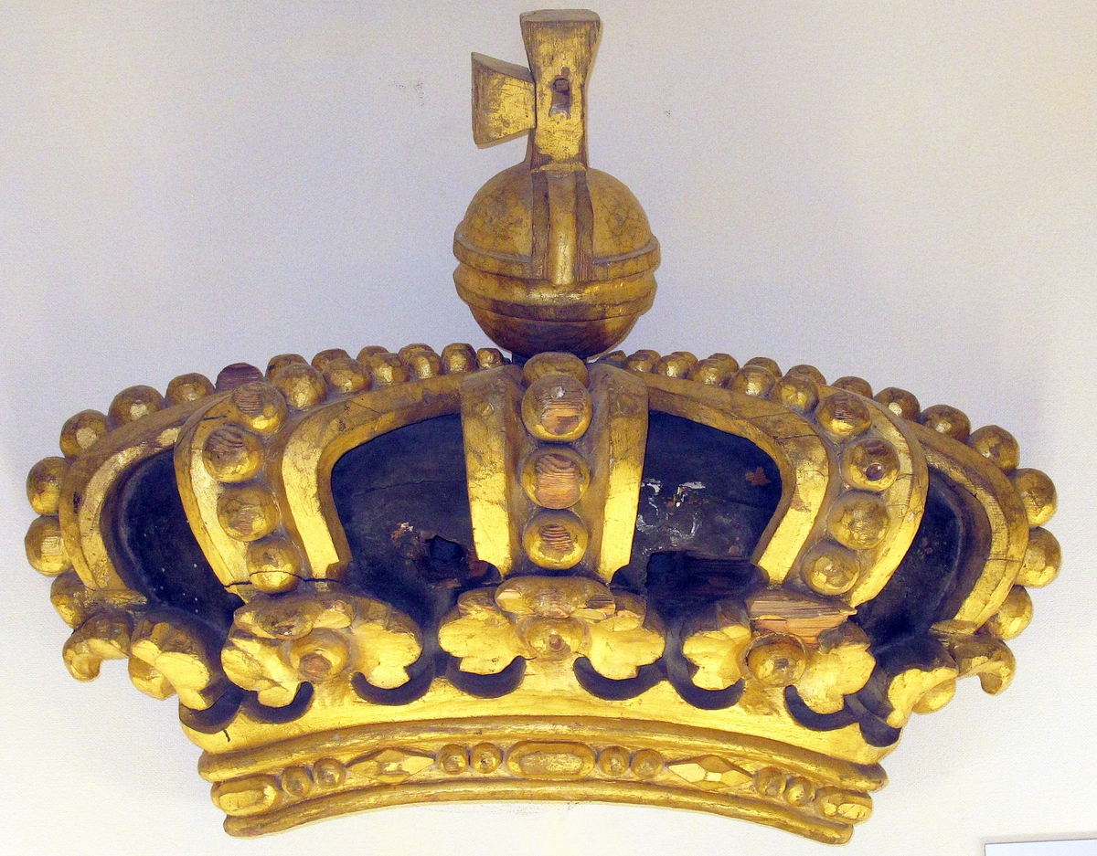 Akterspegelornament tillhörande linjeskeppet KARL XIV JOHAN, bestående av sköld, krona med äpple. Ej konserverad
a) Sköld cirkelrund med Karl XIV Johans namnschiffer, förgylld på blå refflad botten. Kantlisten förgylld. Märkt: ?50? på vidhäftad plåt. Diameter max 1085 mm Diameter min. 1050 mm
b) krona, kunglig förgylld med svart botten, två bulthål. Bredd: 850 mm. Höjd: 390 mm
c) Äpple med kors, förgylld, deffekt. Höjd med fästlapp: 350 mm. Diameter: 160 mm.