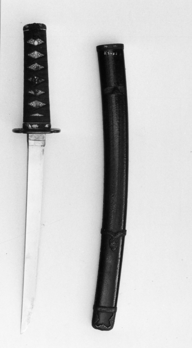 Samurai-dolk (WAKICACHI) från Japan. Klinga svagt bakåtböjd,eneggad, skarp, facetterad rygg. Fäste av vitt hajskinn flätat med grönt bomullsband med två amuletter, delvis förgyllda. Beslag upptill och nedtill cicilerade och förgyllda. Parerplåt rund med ett hål på ena sidan samt med förgyllt och cicilerat bladverk. Balja av trä, svartlackerad med beslag å fyra ställen.
Låsfjädern,d.v.s. bestickknivens handtag saknas.
Kniven på baljan (KOZUKA) saknas.
Från fregatten VANADIS världsomsegling 1883-85.