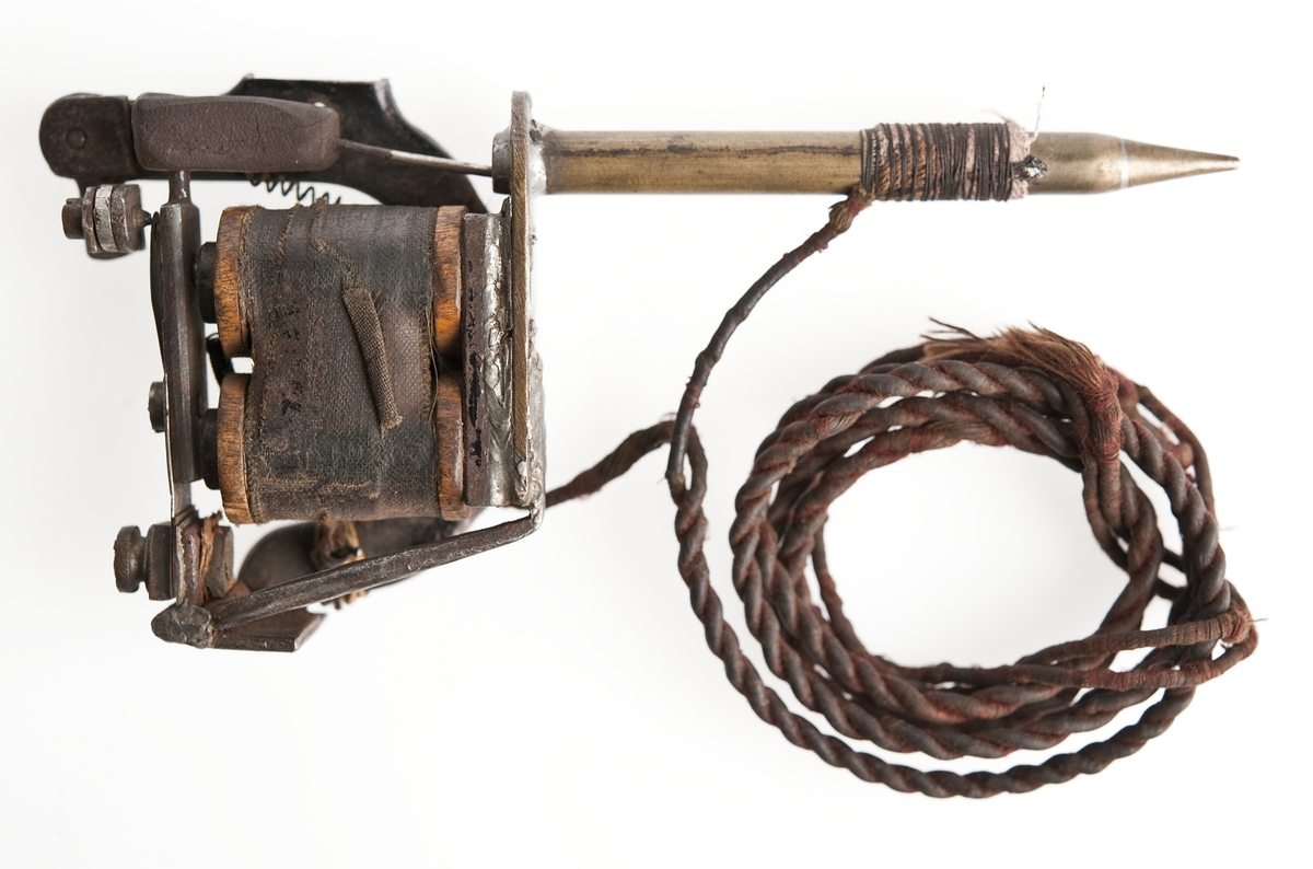 Tatueringsapparat som drivs med en elektrisk motor. Kom till museet 1934.