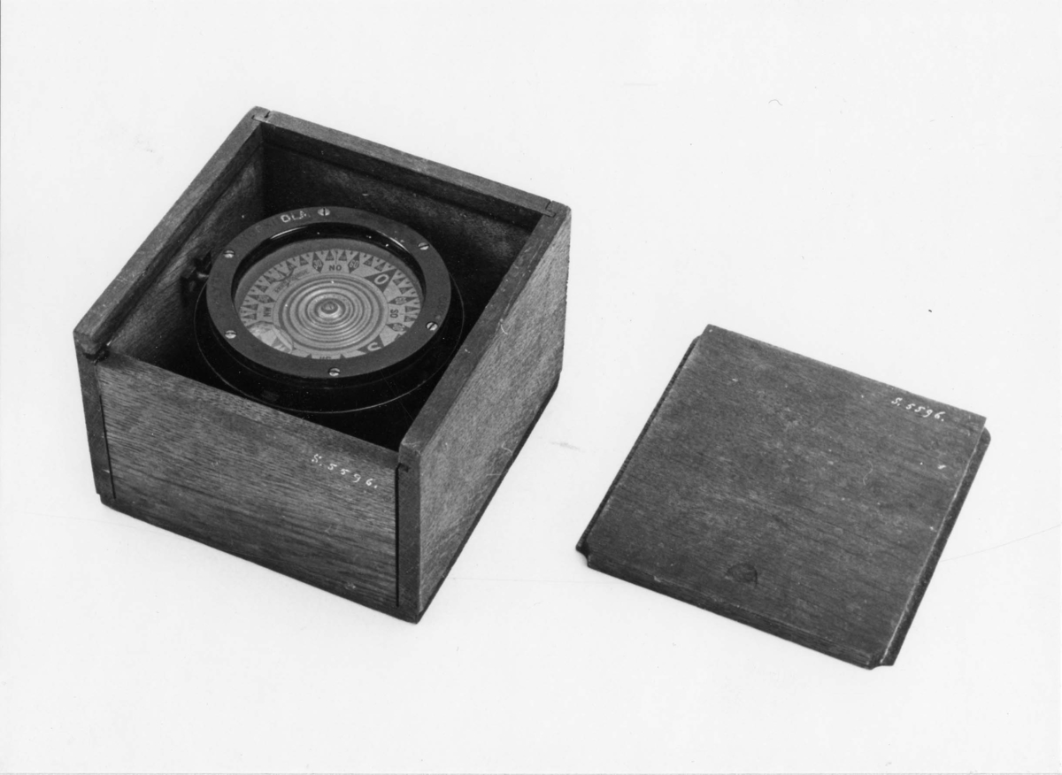 3,5 tums båtkompass, graderad i interkardinalstreck och 5 grader. Kardansk upphängning med röda tappar. Fyrkantig låda av ek med skjutlock.