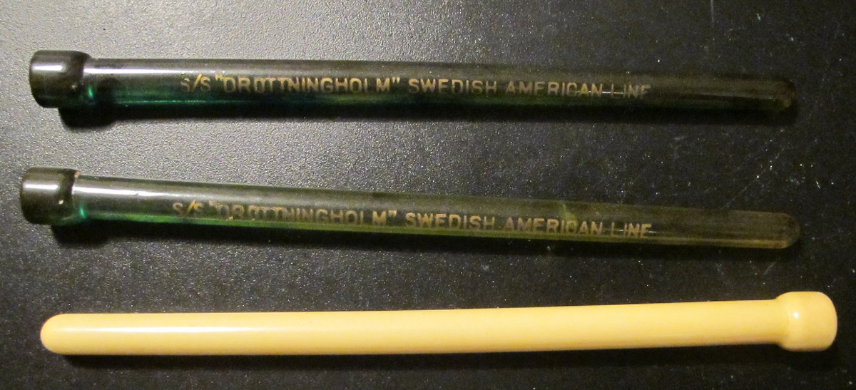 3 st drinkpinnar i benvit (1st) respektive transparent grönt. De två gröna med texten: "S/S "DROTTNINGHOLM" SWEDISH AMERICAN LINE". Föremålens form: Avlånga, runda