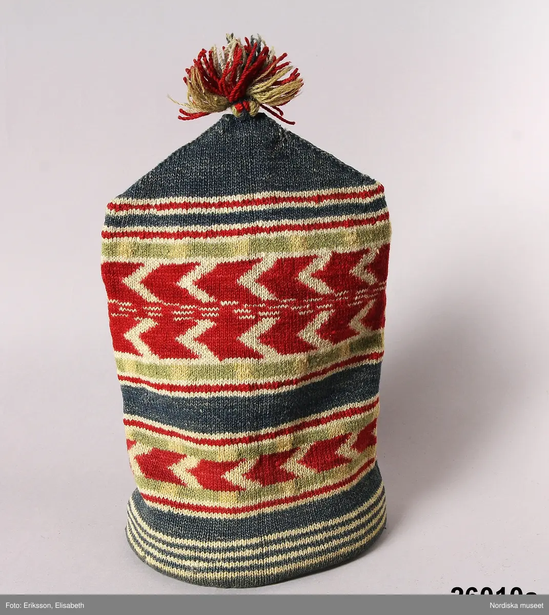 2 st röda toppluvor, A-B.
A.
B.Röd toppluva, maskinstickad i slätstickning av ullgarn, filtad, 2 stycken med nästan osynliga sidsömmar, hoptagningar i toppen. Liten röd ullgarnstofs högst upp. Nederkanten uppvikt 2 varv.

Berit Eldvik okt 2005