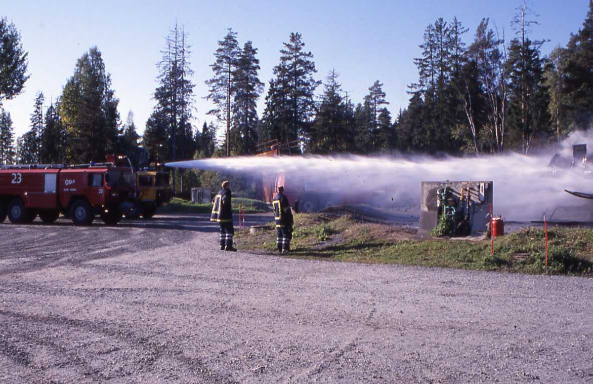 En rød brannbil spruter vann over "øvelse flyet" to brannmenn i front, fra gardermoen flyplass, OSL.